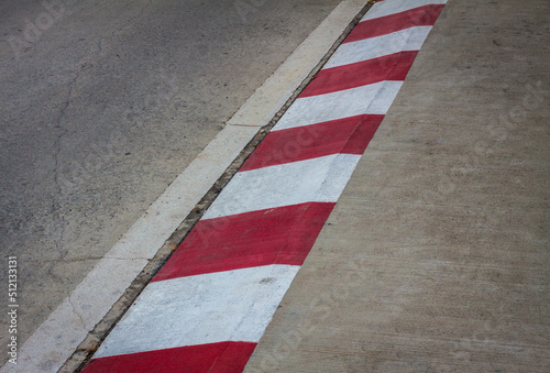Footpath road. Red and white concrete sidewalk curb with green grass. View of Circuit. signs on a road. racetrack with white lines. White and red strip no Parking Sign on Footpath road. © bOnTrue