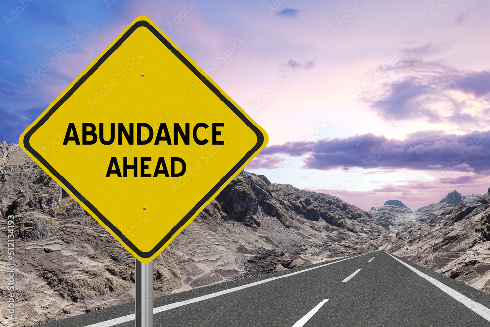 Yellow highway sign with the word Abundance and a metaphoric road leading to future success.