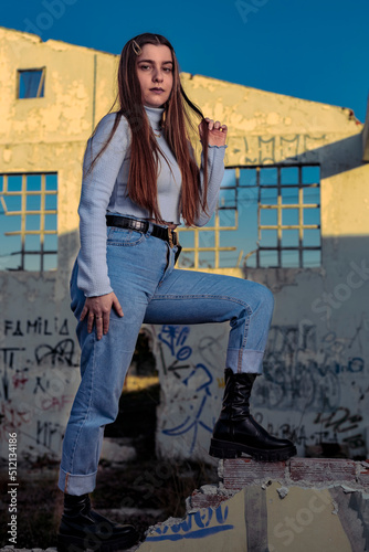 Young blonde model wearing blue pants in an abandoned factory during sunset