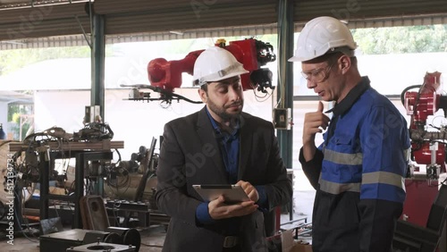 Manager holding tablet talk to robotic engineer to check robotic arm's workflow in the factory.