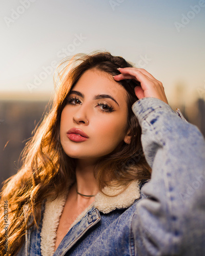 portrait of a young woman in front of a skyline in jeans jacket at sunset