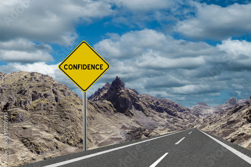 Sign with the word Confidence and a road running through the mountains to the horizon. Motivation concept for manifesting what we want in life.