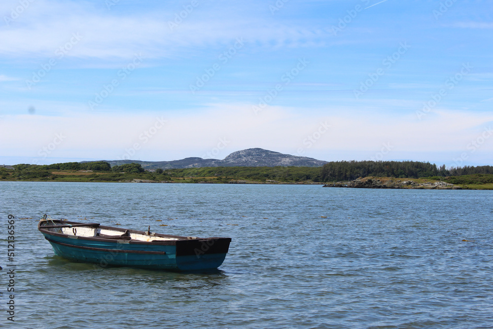 small boat on the calm irish sea in snowdonia, wales with welsh hill landscape in the background 