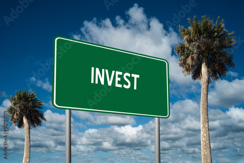 Highway sign with the word Invest on a beautiful blue sky background with palm trees.  Motivational concept for finding what we want on the journey of life.