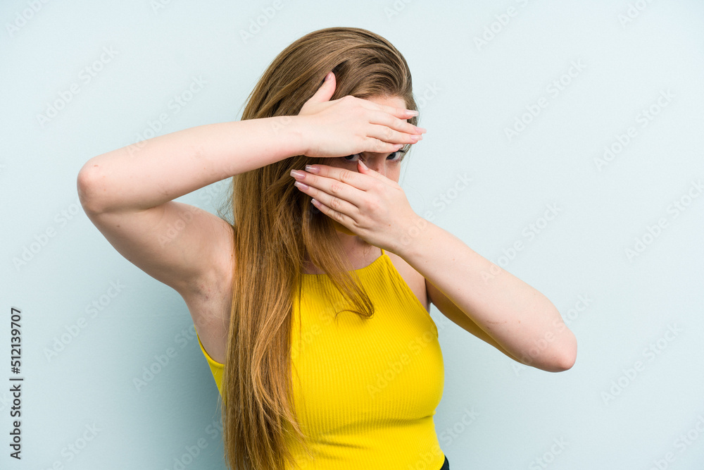 Young caucasian woman isolated on blue background blink at the camera through fingers, embarrassed covering face. Young caucasian woman isolated on blue background blink at the camera through fingers, embarrassed covering face.