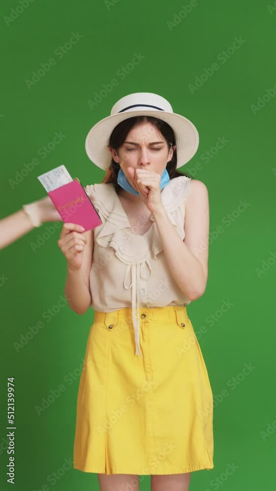 Canceled trip. Travel ban. Covid-19 danger. Happy woman coughing bad unrecognizable hand taking out foreign id tickets covering up medicine mask isolated on green chromakey vertical. Canceled trip. Travel ban. Covid-19 danger. Happy woman coughing bad unrecognizable hand taking out foreign id tickets covering up medicine mask isolated on green chromakey vertical.
