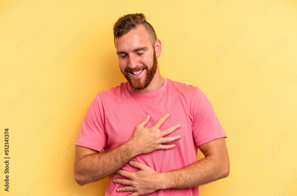 Young caucasian man isolated on yellow background laughs happily and has fun keeping hands on stomach. Young caucasian man isolated on yellow background laughs happily and has fun keeping hands on stomach.