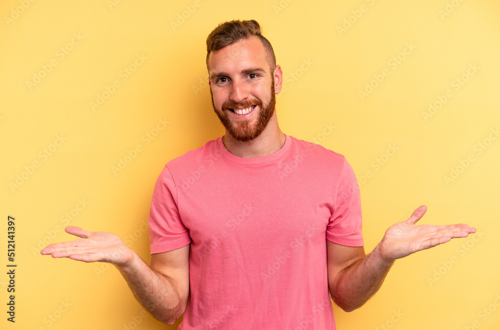 Young caucasian man isolated on yellow background makes scale with arms, feels happy and confident. Young caucasian man isolated on yellow background makes scale with arms, feels happy and confident.