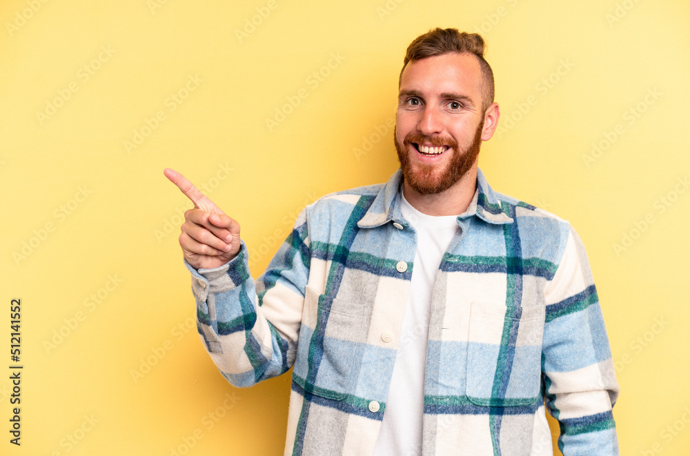 Young caucasian man isolated on yellow background smiling cheerfully pointing with forefinger away. Young caucasian man isolated on yellow background smiling cheerfully pointing with forefinger away.