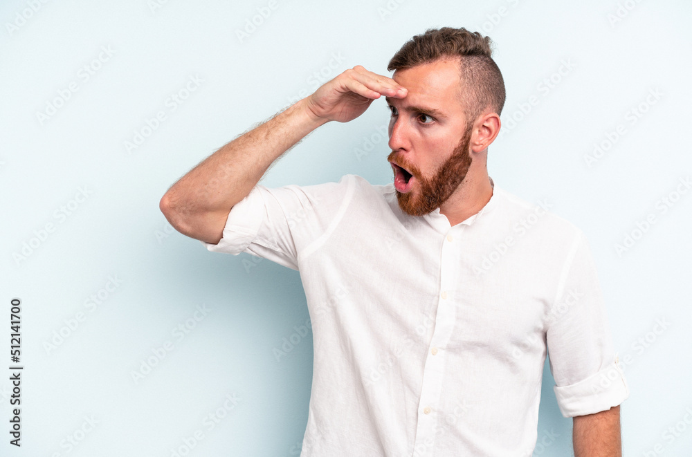 Young caucasian man isolated on blue background looking far away keeping hand on forehead. Young caucasian man isolated on blue background looking far away keeping hand on forehead.