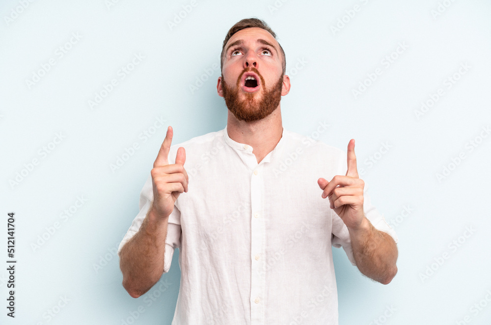 Young caucasian man isolated on blue background pointing upside with opened mouth. Young caucasian man isolated on blue background pointing upside with opened mouth.
