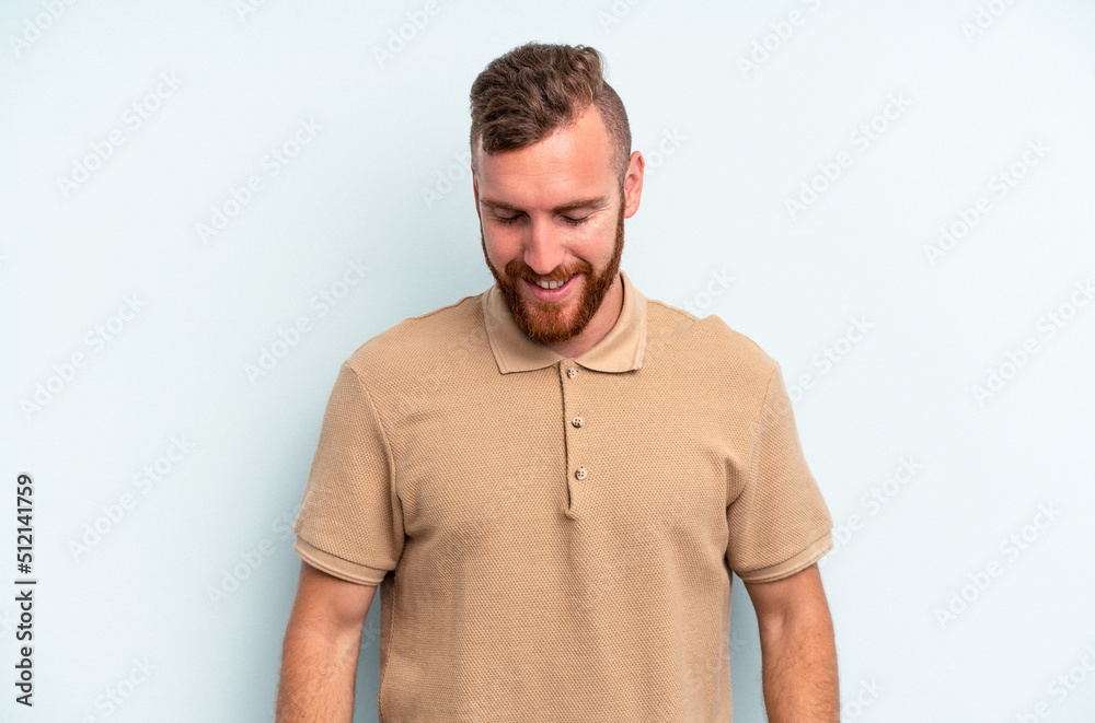 Obraz premium Young caucasian man isolated on blue background laughs and closes eyes, feels relaxed and happy.
