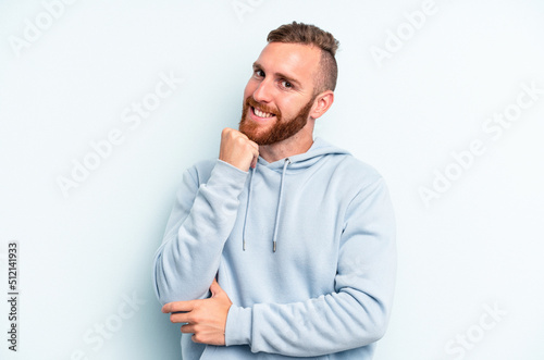 Young caucasian man isolated on blue background smiling happy and confident, touching chin with hand. © Asier