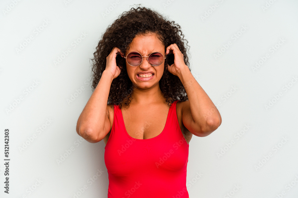 Young brazilian woman wearing a swimsuit isolated on blue background covering ears with hands. Young brazilian woman wearing a swimsuit isolated on blue background covering ears with hands.