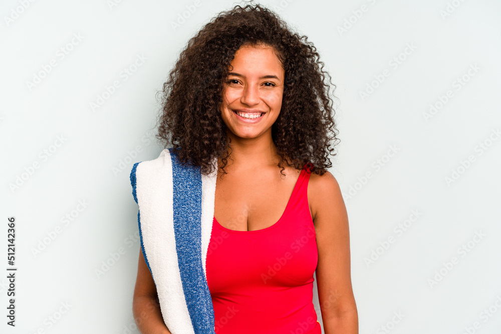 Young brazilian woman going to the beach holding a towel isolated on blue background happy, smiling and cheerful. Young brazilian woman going to the beach holding a towel isolated on blue background happy, smiling and cheerful.