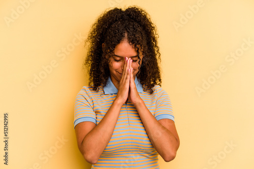 Billede på lærred Young Brazilian woman isolated on yellow background praying, showing devotion, religious person looking for divine inspiration