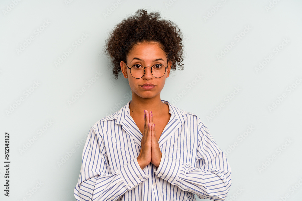 Young Brazilian woman isolated on blue background praying, showing devotion, religious person looking for divine inspiration. Young Brazilian woman isolated on blue background praying, showing devotion, religious person looking for divine inspiration.