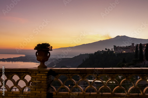 Scenic view on snow capped Mount Etna volcano and Mediterranean sea during sunset from public garden Parco Duca di Cesaro to Giardini Naxos in Taormina, Sicily, Italy, Europe, EU. Silhouette railing photo