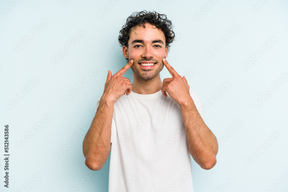 Young caucasian man isolated on blue background smiles, pointing fingers at mouth. Young caucasian man isolated on blue background smiles, pointing fingers at mouth.
