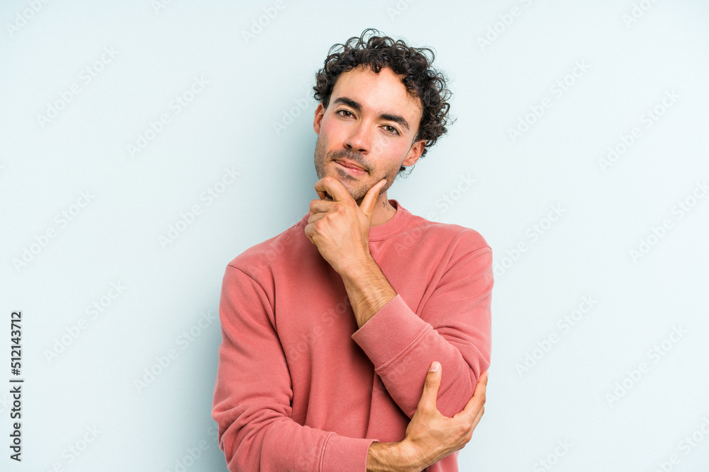 Young caucasian man isolated on blue background suspicious, uncertain, examining you.