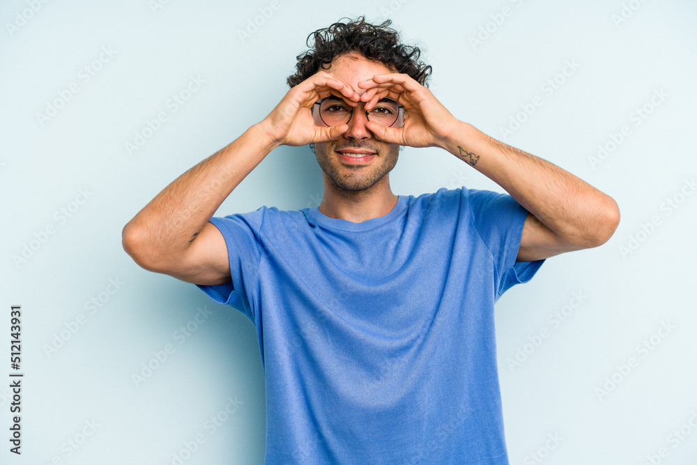 Young caucasian man isolated on blue background showing okay sign over eyes Young caucasian man isolated on blue background showing okay sign over eyes