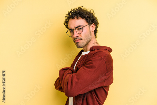 Young caucasian man isolated on yellow background frowning face in displeasure  keeps arms folded.