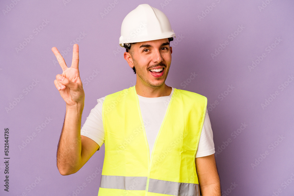 Young hispanic worker man isolated on purple background joyful and carefree showing a peace symbol with fingers. Young hispanic worker man isolated on purple background joyful and carefree showing a peace symbol with fingers.