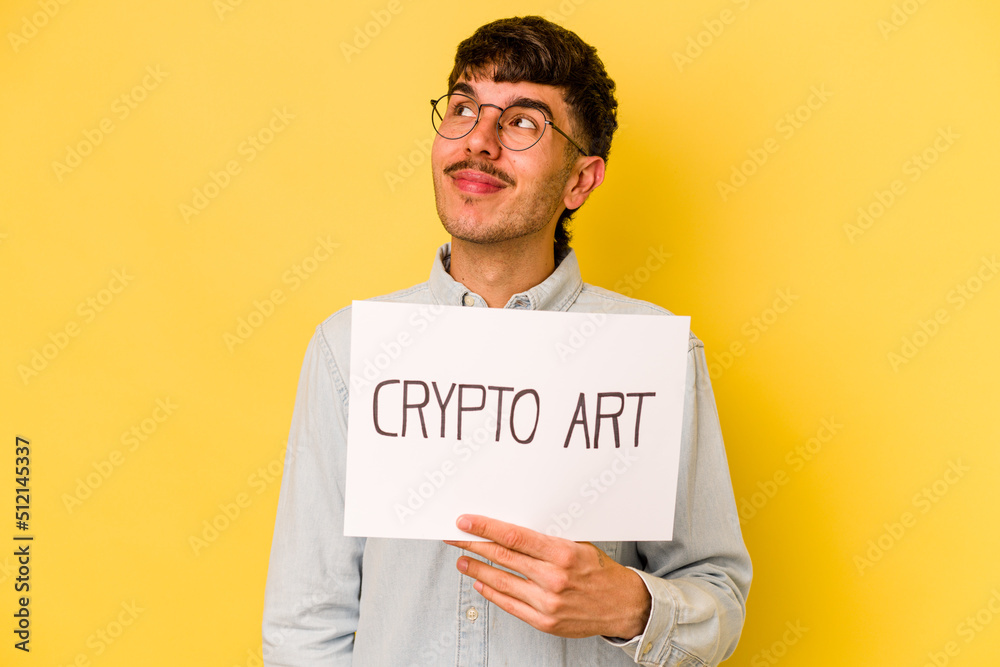 Young hispanic man holding crypto art placard isolated on yellow background dreaming of achieving goals and purposes Young hispanic man holding crypto art placard isolated on yellow background dreaming of achieving goals and purposes