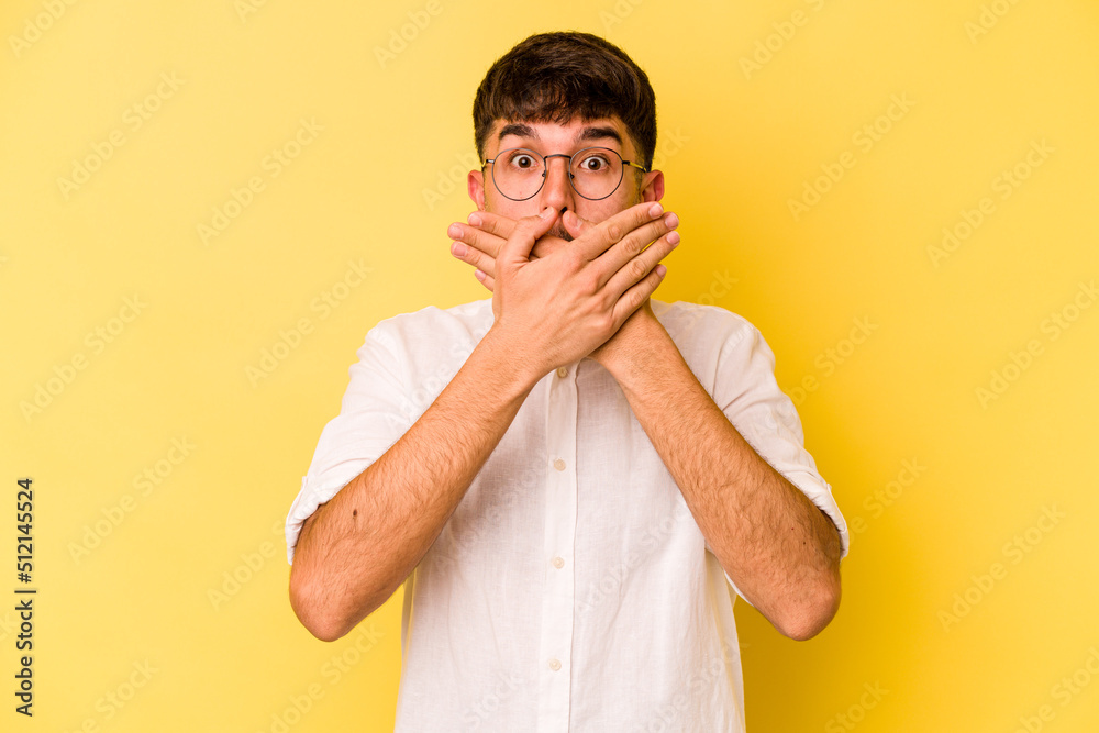Young caucasian man isolated on yellow background shocked covering mouth with hands. Young caucasian man isolated on yellow background shocked covering mouth with hands.