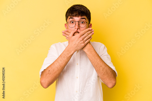 Young caucasian man isolated on yellow background shocked covering mouth with hands.