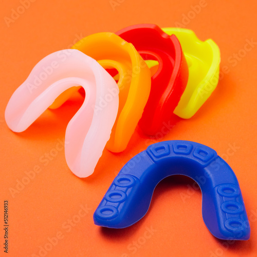 many colored boxing mouth guards lie on an orange background, concept photo