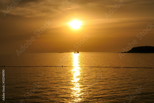 Romantic sunset by a beach. The sun sets over the horizon. The sun beams reflecting in the calm sea waters. There is an island on the side. Few birds flying around. The sky turns yellow and orange © Chris