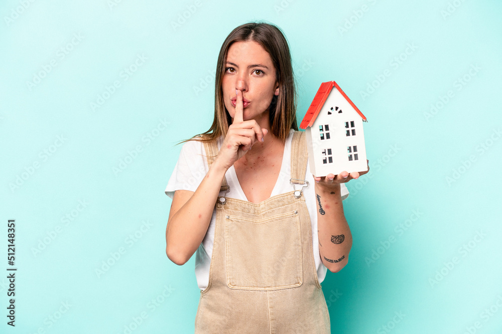 Young caucasian pregnant woman holding an toy house isolated on blue background keeping a secret or asking for silence. Young caucasian pregnant woman holding an toy house isolated on blue background keeping a secret or asking for silence.