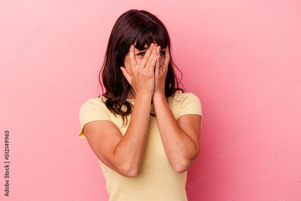 Young caucasian woman isolated on pink background blink at the camera through fingers, embarrassed covering face. Young caucasian woman isolated on pink background blink at the camera through fingers, embarrassed covering face.