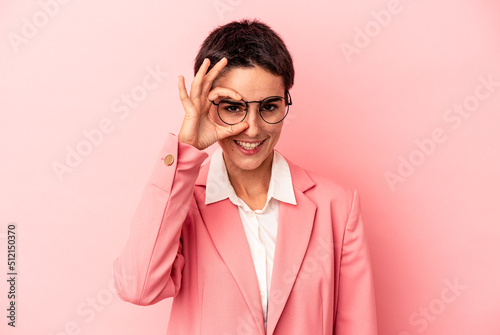 Young business woman wearing a pink blazer isolated on pink background excited keeping ok gesture on eye.