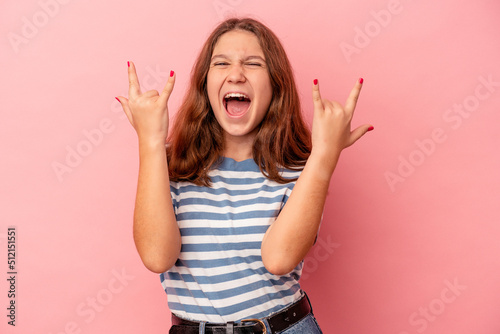 Little caucasian girl isolated on pink background showing a horns gesture as a revolution concept.