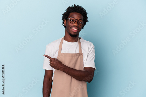 Foto Young african american store clerk isolated on blue background smiling and pointing aside, showing something at blank space