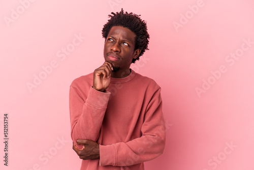 Young african american man isolated on pink background thinking and looking up, being reflective, contemplating, having a fantasy. © Asier