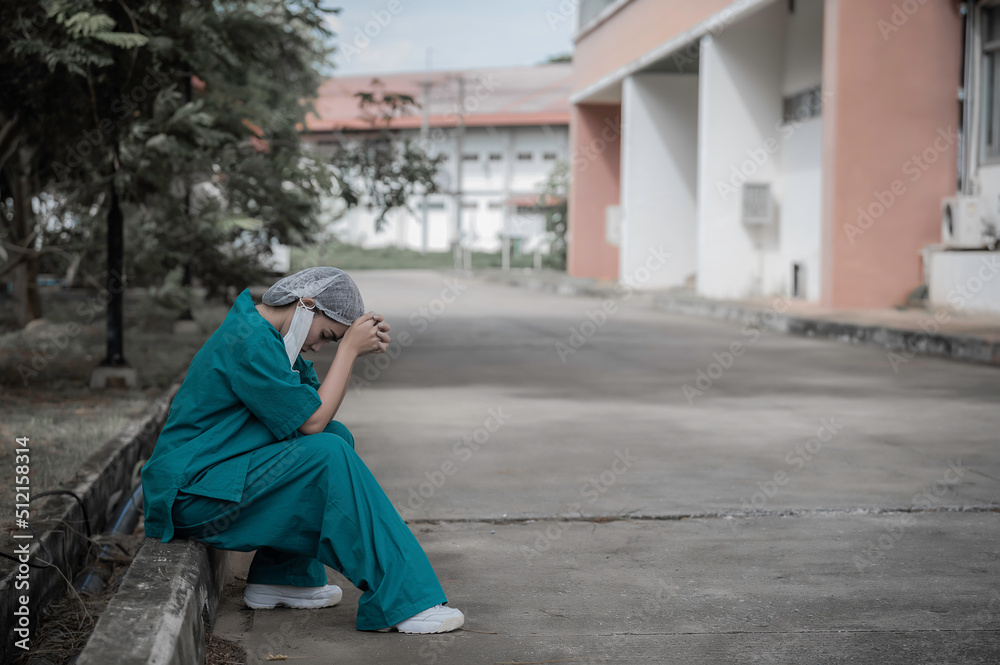 Naklejka premium Tired depressed female asian scrub nurse wears face mask blue uniform sits on hospital floor,Young woman doctor stressed from hard work