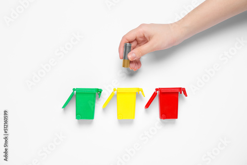 Woman throwing battery into trash bin on white background, top view