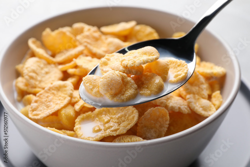 Spoon with tasty cornflakes and milk over bowl  closeup