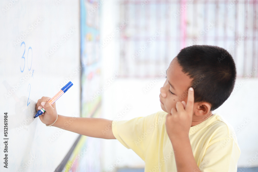 Fototapeta premium Asian kid doing multiplication math on white board in learning activity