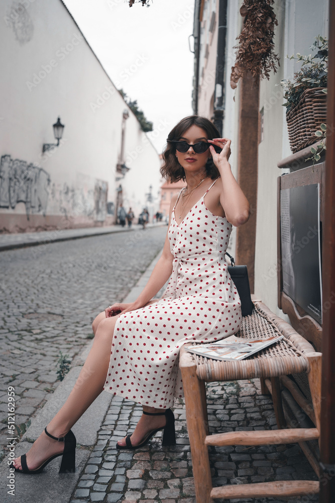 Female sitting on a bench in the historic streets of Prague holding her sunglasses