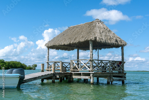 Wooden bungalow set on the water. Pavilion with thatched roof on turquoise water. Sea pier. Boat station.