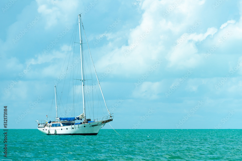 Lonely sailboat on a turquoise sea surface. Yacht with folded sail. Sailboat in calm weather, against the background of a cloudy sky.