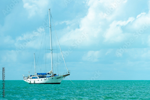 Lonely sailboat on a turquoise sea surface. Yacht with folded sail. Sailboat in calm weather, against the background of a cloudy sky.