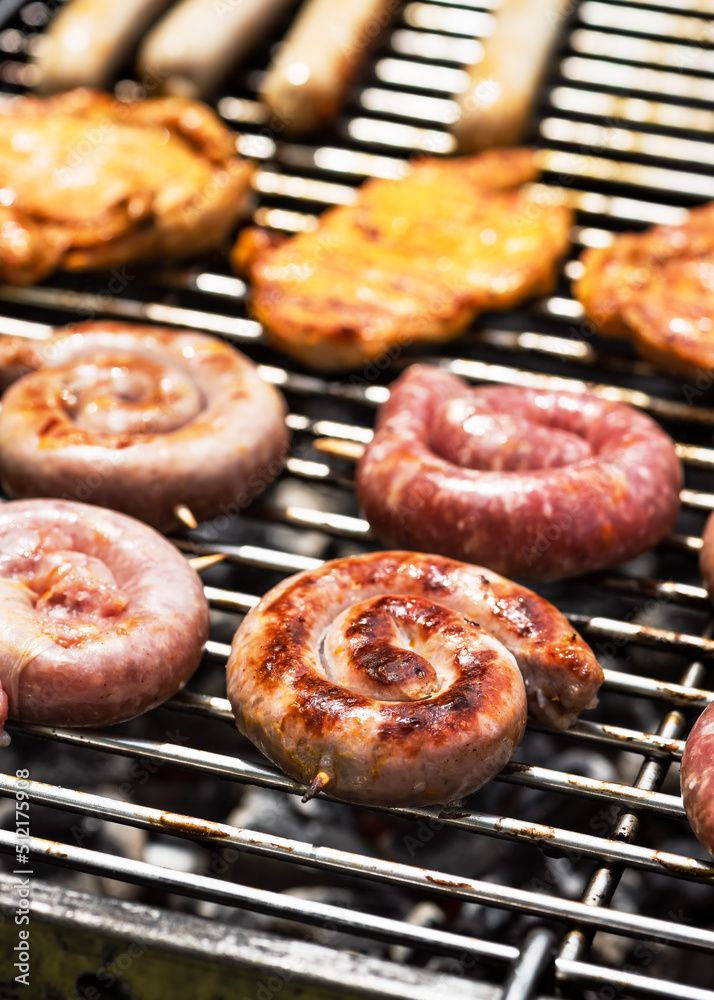 Spirals of spicy sausage grilling on a barbecue grilling over the hot coals outdoors in the garden or park on a summer picnic. Selective focus. Spirals of spicy sausage grilling on a barbecue grilling over the hot coals outdoors in the garden or park on a summer picnic. Selective focus.