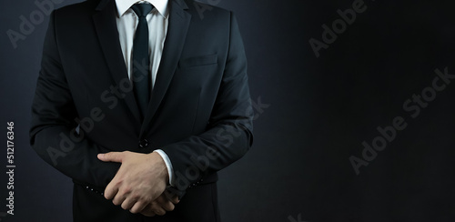 A man in a suit with folded hands at the waist on a black background. Сopyspace