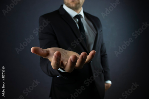 Male hand in a suit shows a palm up gesture on a black background. Concept of request, bankruptcy, close-up.