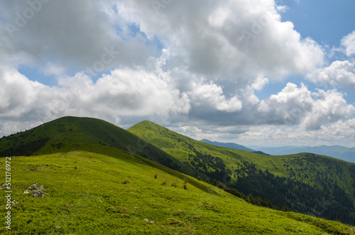 Beautiful ridge of mountains with lush green grass on tops and slopes on background of blue sky with clouds. Carpathians, Ukraine